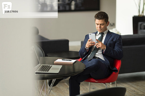 Geschäftsmann sitzt im Büro und schaut auf sein Smartphone