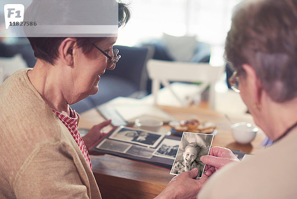 Über-Schulter-Ansicht von zwei älteren Frauen  die sich alte Fotos bei Tisch anschauen