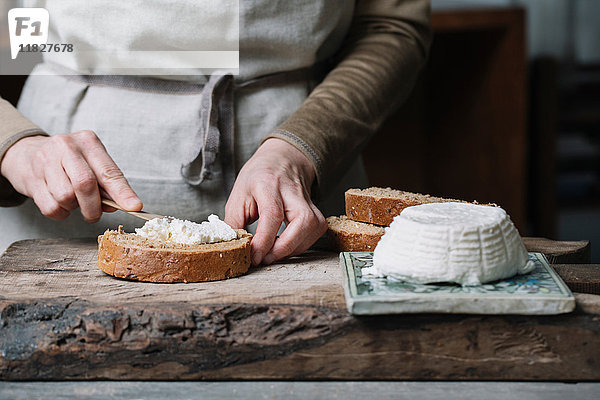 Frau streicht Ricotta-Käse auf Brotscheibe  mittlerer Abschnitt