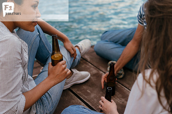 Drei Freunde entspannen sich am Pier und halten Bierflaschen