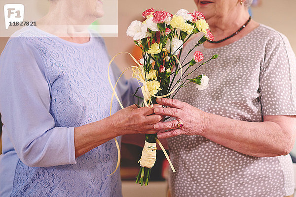 Ältere Frau überreicht Freundin Blumen auf Geburtstagsfeier