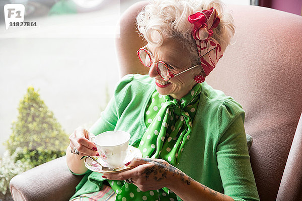 Fröhliche schrullige reife Frau mit Teetasse und Untertasse in der Hand in der Teestube