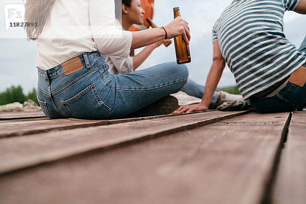 Drei Freunde entspannen sich am Pier  halten Bierflaschen in der Hand  niedriger Abschnitt