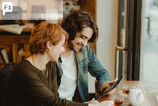 Junges Paar sitzt im Café und schaut auf ein digitales Tablett
