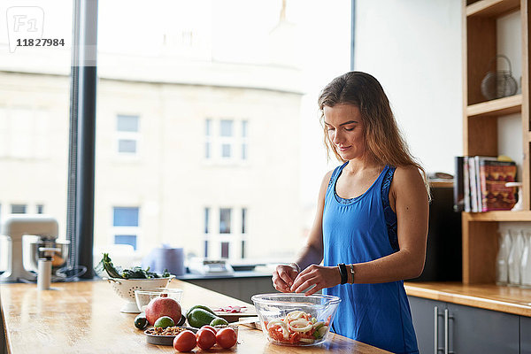 Junge Frau am Küchentisch beim Zubereiten der Salatschüssel