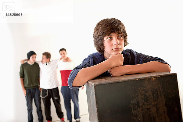 Teenager  der sich mit Freunden im Hintergrund an eine Kiste lehnt