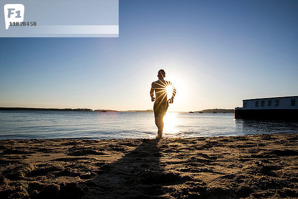 Hinterleuchteter junger männlicher Läufer läuft bei Sonnenuntergang am Strand