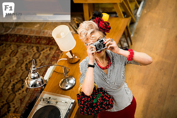 Schrullige Frau fotografiert mit einer Oldtimer-Kamera im Antiquitätenladen