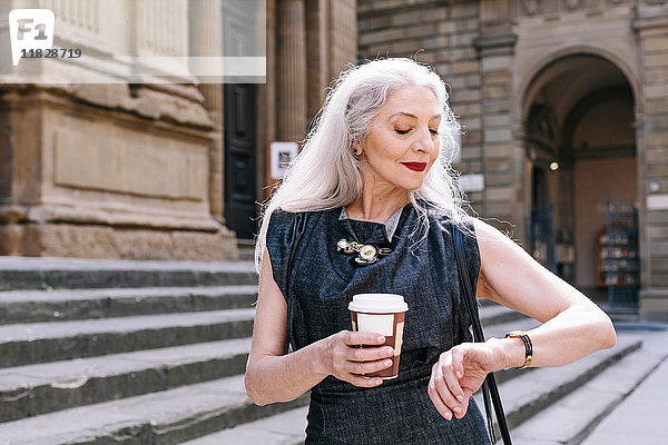 Reife Frau mit langen grauen Haaren schaut auf Armbanduhr in Florenz  Italien
