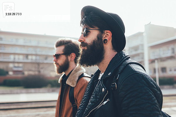 Seitenansicht von zwei jungen männlichen Hipster-Freunden mit Sonnenbrille in einer städtischen Wohnsiedlung
