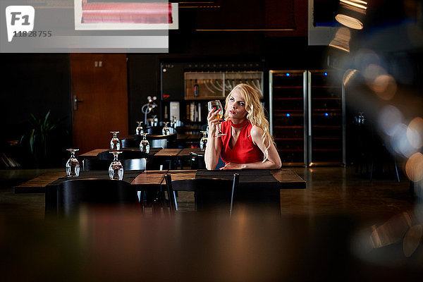 Glamouröse junge Frau mit langen blonden Haaren sitzt allein am Restauranttisch