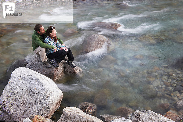 Mittelgroßes erwachsenes Paar sitzt auf Felsen im Fluss