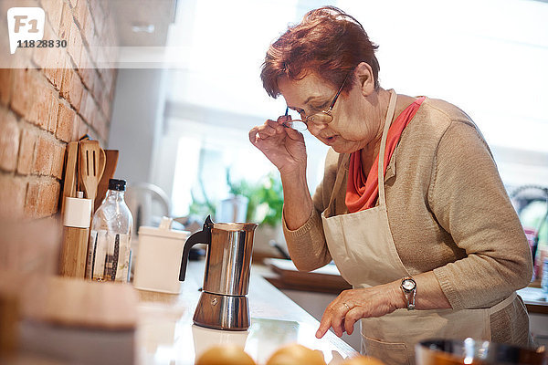 Ältere erwachsene Frau  die lernt  ein Elektrokochfeld zum Kaffee kochen zu benutzen