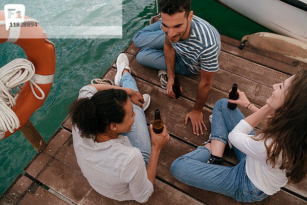 Drei Freunde entspannen sich am Pier  halten Bierflaschen in der Hand  erhöhte Ansicht