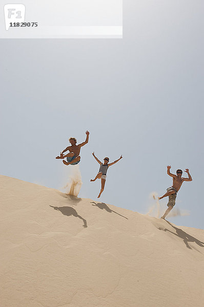 Freunde springen über eine große Sanddüne