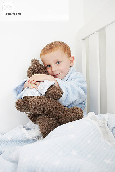 Junge umarmt Teddybär im Bett