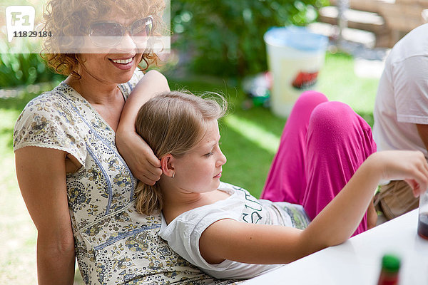 Mädchen ruht auf der Mutter bei Tisch im Freien