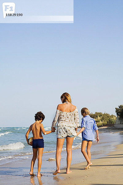 Frau geht mit Kindern am Strand spazieren