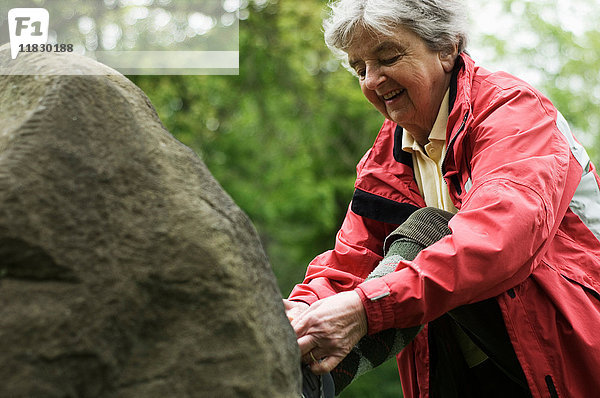 Ältere Frau beim Schuhbinden auf einem Felsen im Park