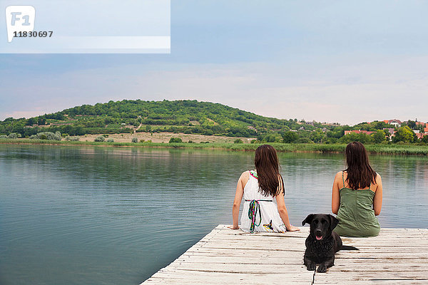 Frauen sitzen mit Hund am Pier