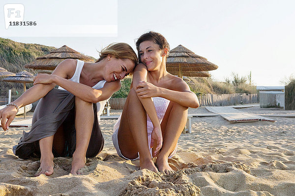 Zwei glückliche Frauen sitzen auf Sand am Strand