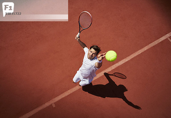 Overhead-Ansicht junger Tennisspieler  der Tennis spielt und den Ball auf dem sonnigen Tennisplatz serviert.