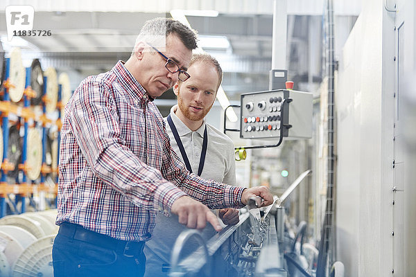 Männlicher Supervisor und Arbeiter  der die Maschinen in der Glasfaserfabrik untersucht.