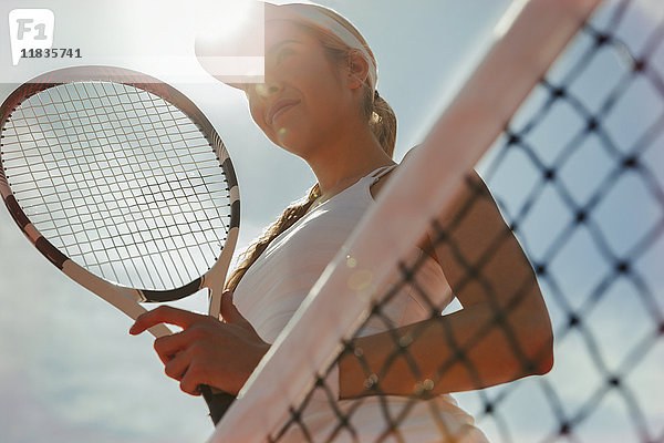 Selbstbewusste junge Tennisspielerin mit Tennisschläger am Netz
