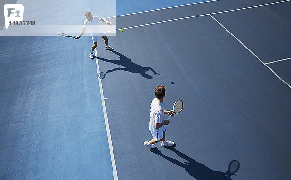 Junge Männer verdoppeln Tennisspieler beim Tennisspielen auf dem sonnigen blauen Tennisplatz