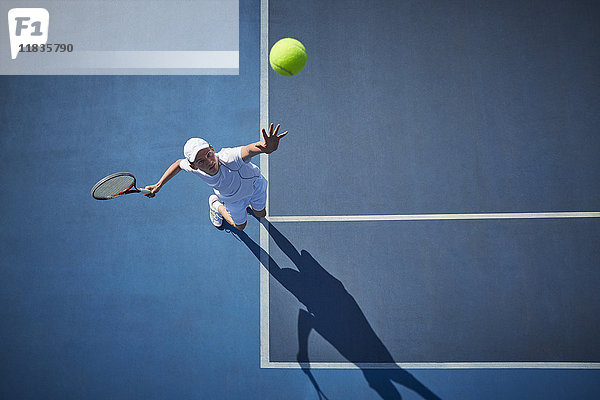 Draufsicht auf den jungen Tennisspieler  der Tennis spielt und den Ball auf dem sonnigen blauen Tennisplatz serviert.