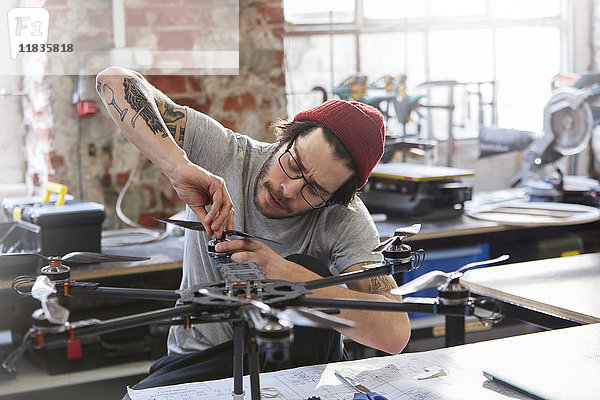 Männlicher Designer mit Tätowierungen und Drohne in der Werkstatt