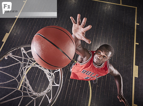 Overhead-Ansicht junger männlicher Basketballspieler  der springt  um den Ball auf die Basketballfelge zu prallen.