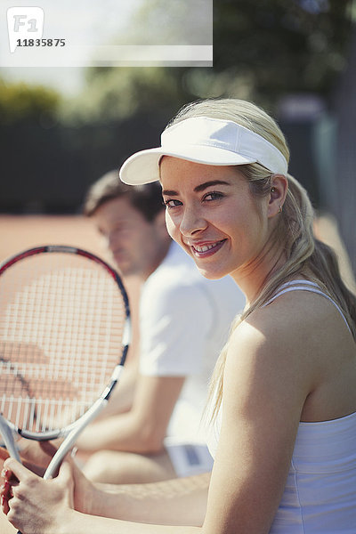 Portrait lächelnde  selbstbewusste junge Tennisspielerin mit Tennisschläger auf sonnigem Tennisplatz