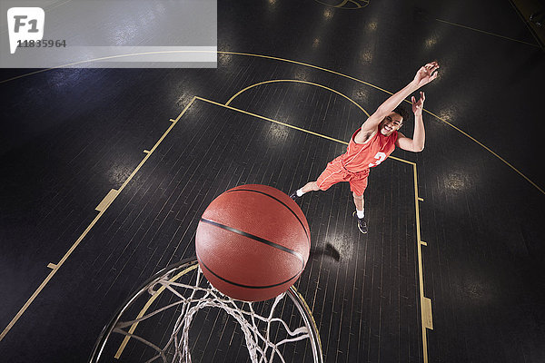 Junger Basketballspieler  der den Ball auf dem Platz in der Turnhalle schießt.