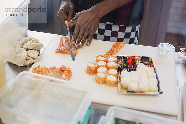 Junge Köchin schneidet Lachs und macht Sushi im Restaurant