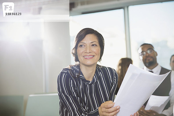 Lächelnde Geschäftsfrau mit Papierkram in Konferenzraumbesprechung