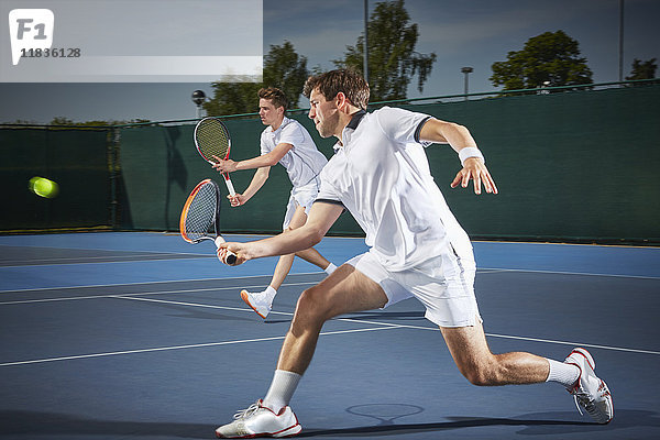 Junge männliche Tennisspieler spielen Tennis  schlagen den Ball auf dem blauen Tennisplatz.