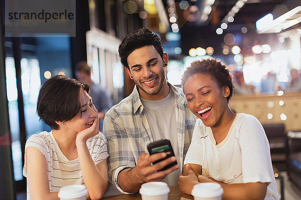 Junge Freunde benutzen ihr Handy  schreiben SMS und lachen im Café