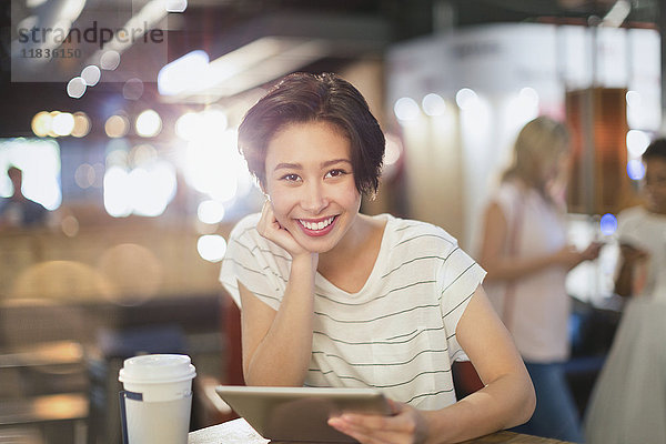 Porträt einer lächelnden jungen Frau  die ein digitales Tablet benutzt und in einem Café Kaffee trinkt