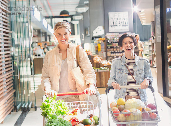 Lächelnde junge Frauen schieben Einkaufswagen im Lebensmittelmarkt