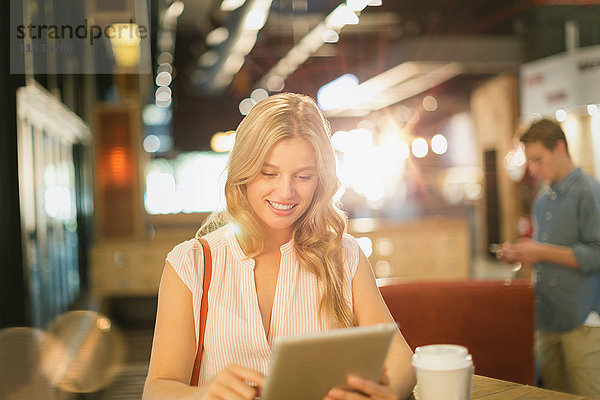 Lächelnde junge Frau  die ein digitales Tablet benutzt und Kaffee in einem Café trinkt