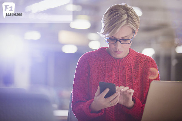 Geschäftsfrau arbeitet spät am Laptop  SMS mit Handy im dunklen Büro