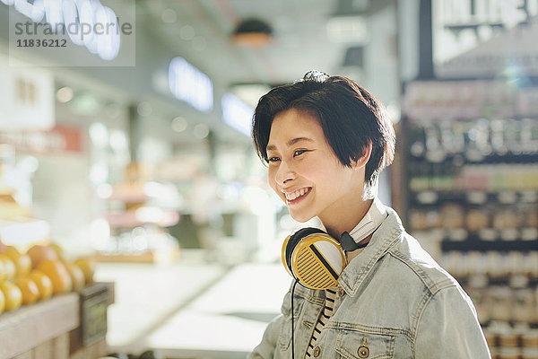 Lächelnde junge Frau mit Kopfhörern beim Lebensmitteleinkauf auf dem Markt