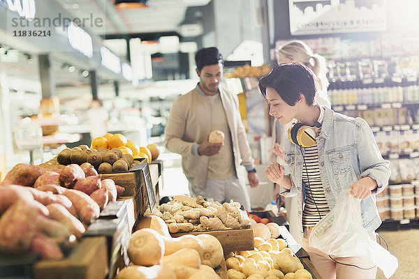 Junge Frau mit Kopfhörern beim Lebensmitteleinkauf und beim Durchstöbern von Produkten auf dem Markt