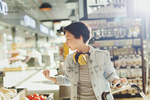 Junge Frau mit Kopfhörern beim Stöbern und Einkaufen im Supermarkt