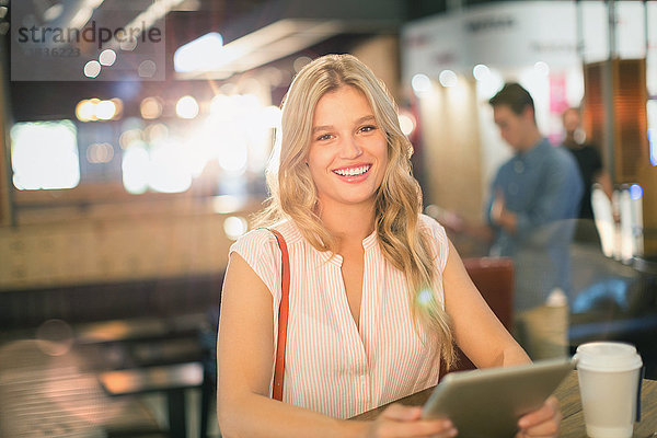 Porträt einer lächelnden jungen Frau  die in einem Café ein digitales Tablet benutzt