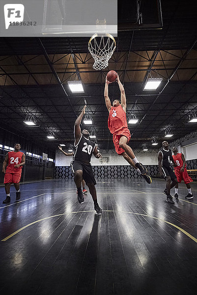 Junger männlicher Basketballspieler  der im Spiel auf dem Platz in der Turnhalle springt  um Basketball zu schlagen.
