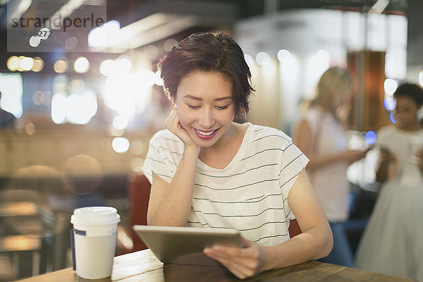 Junge Frau  die ein digitales Tablet benutzt und in einem Café Kaffee trinkt