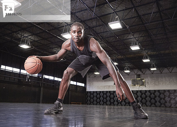 Portrait selbstbewusster junger Basketballspieler  der den Ball auf dem Platz in der Turnhalle dribbelt.