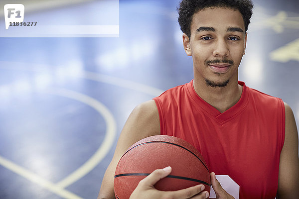 Portrait selbstbewusster junger Basketballspieler mit Basketball auf dem Platz